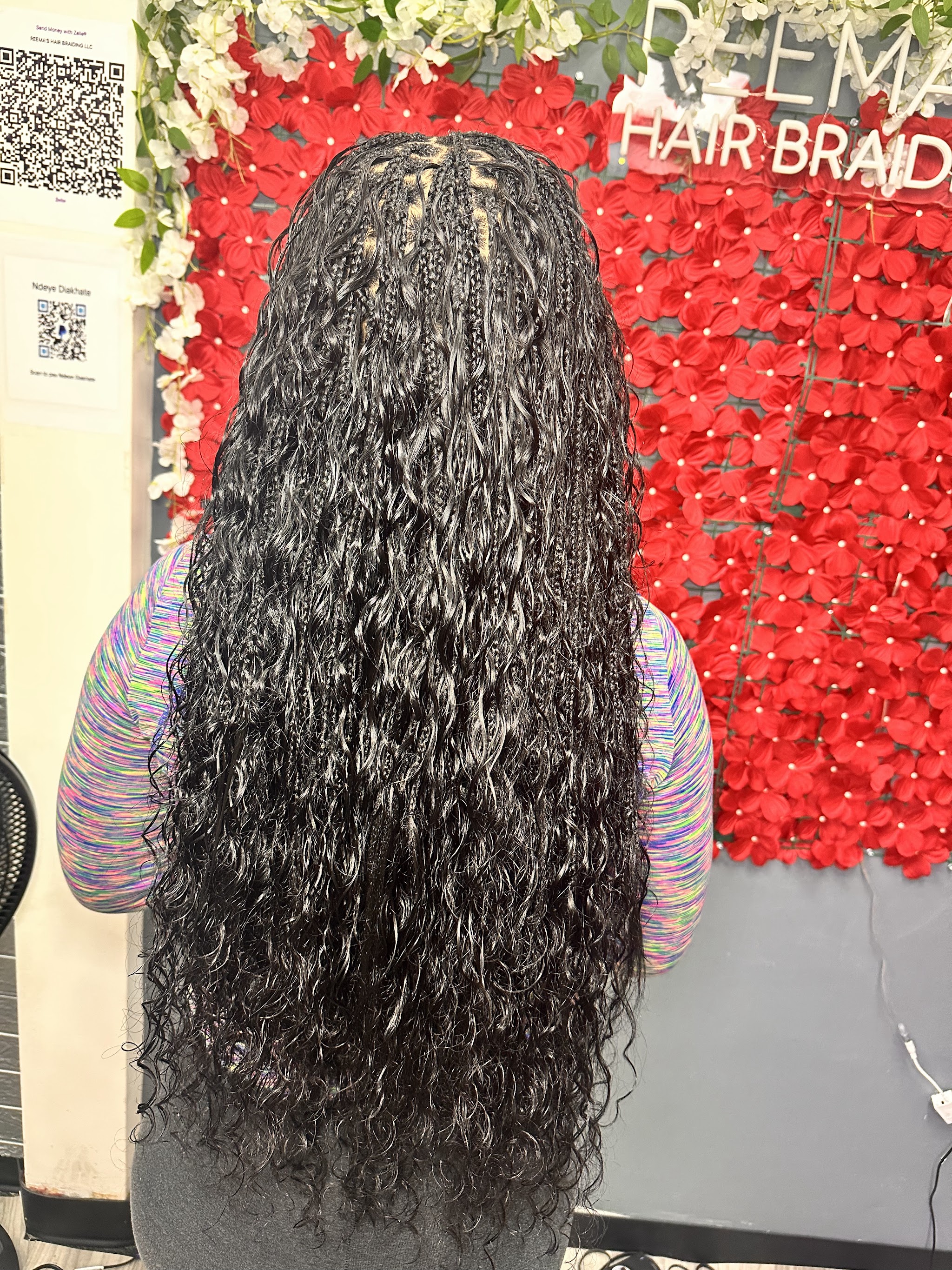 Long boho braids in front of the red flower wall and neon sign at Reema African Hair Braiding